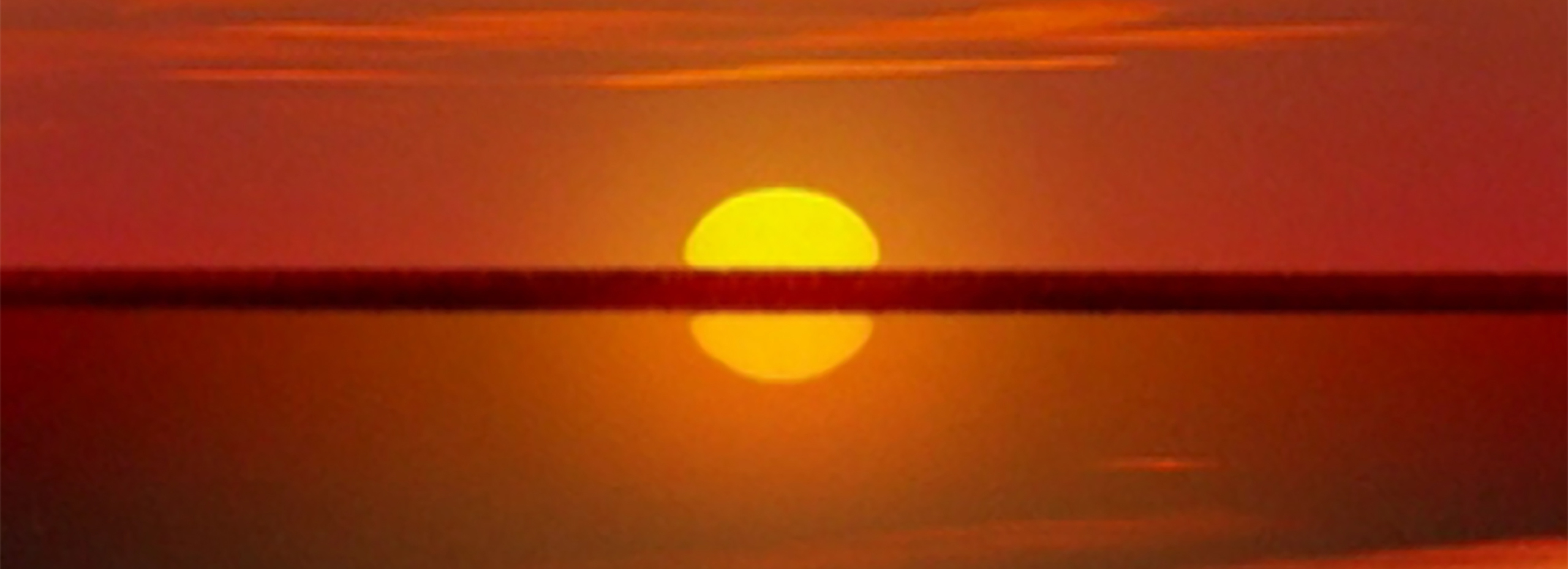 A yellow sun breaks a horizon line with orange sky reflected in water below