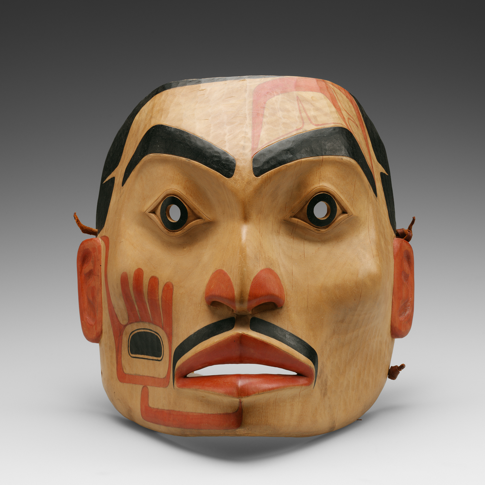 A wood mask painted to look like a human face with dark eyebrows and mustache