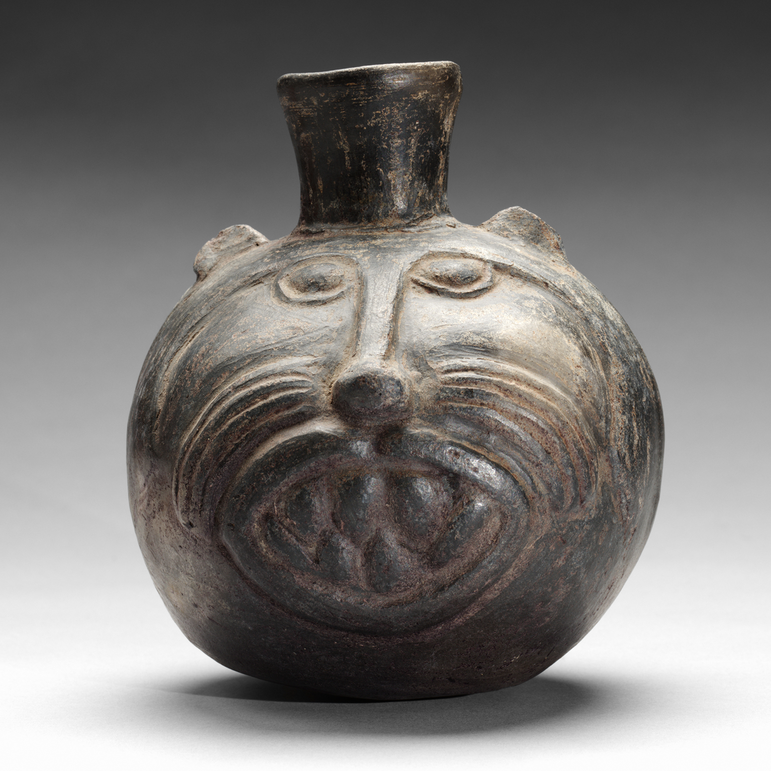A small dark bottle with an incised feline face