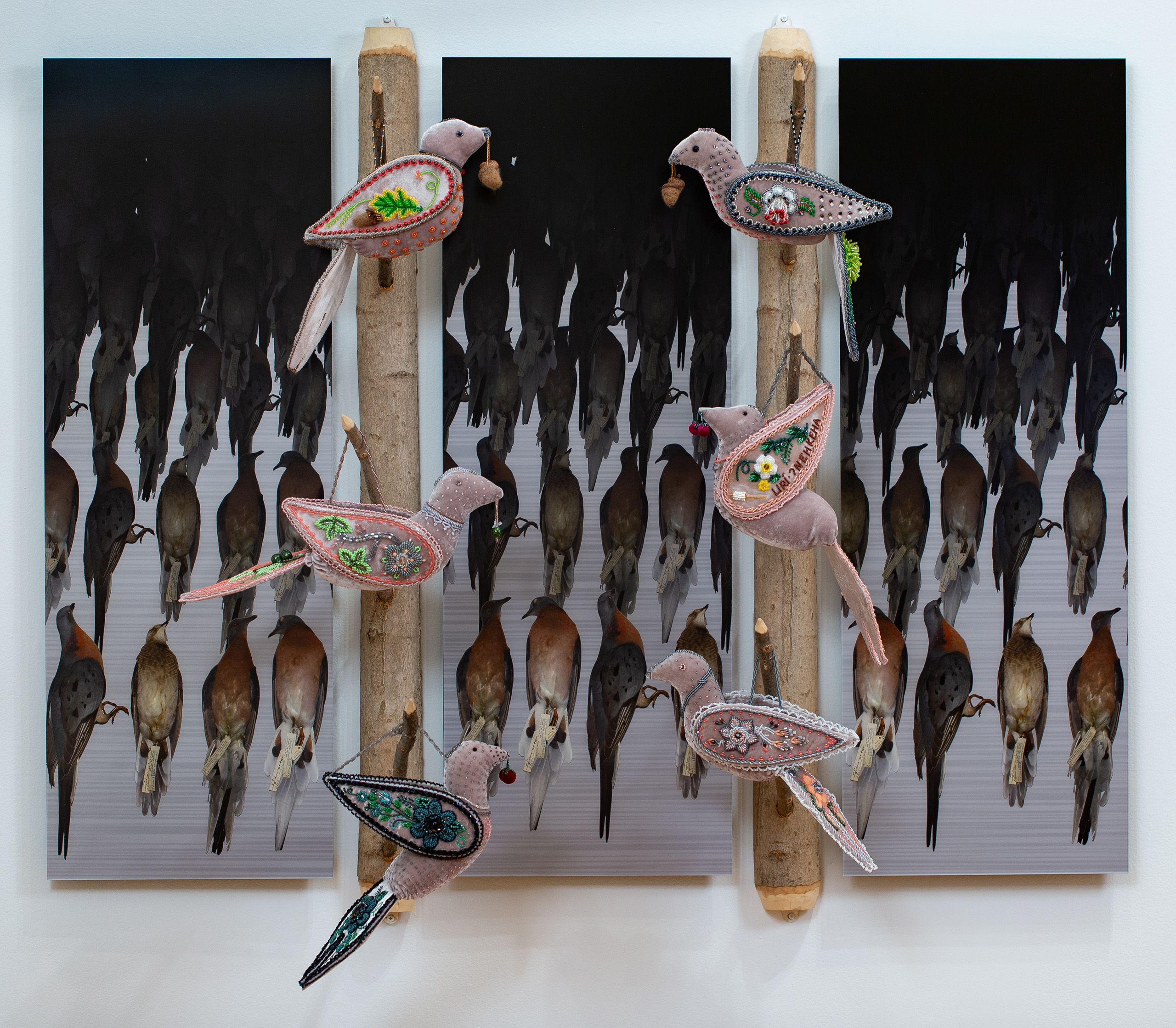 A repeating image of birds fading from color to black is divided into three parts by vertical tree branches on which decorative beaded birds are hung