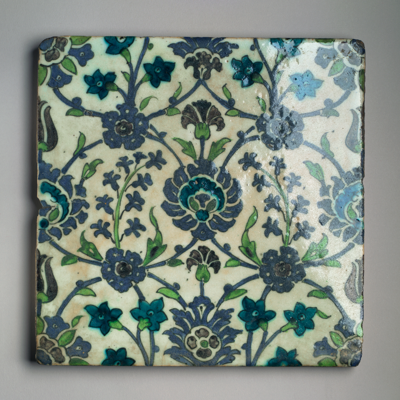 An off-white square tile with floral motifs in blue and green