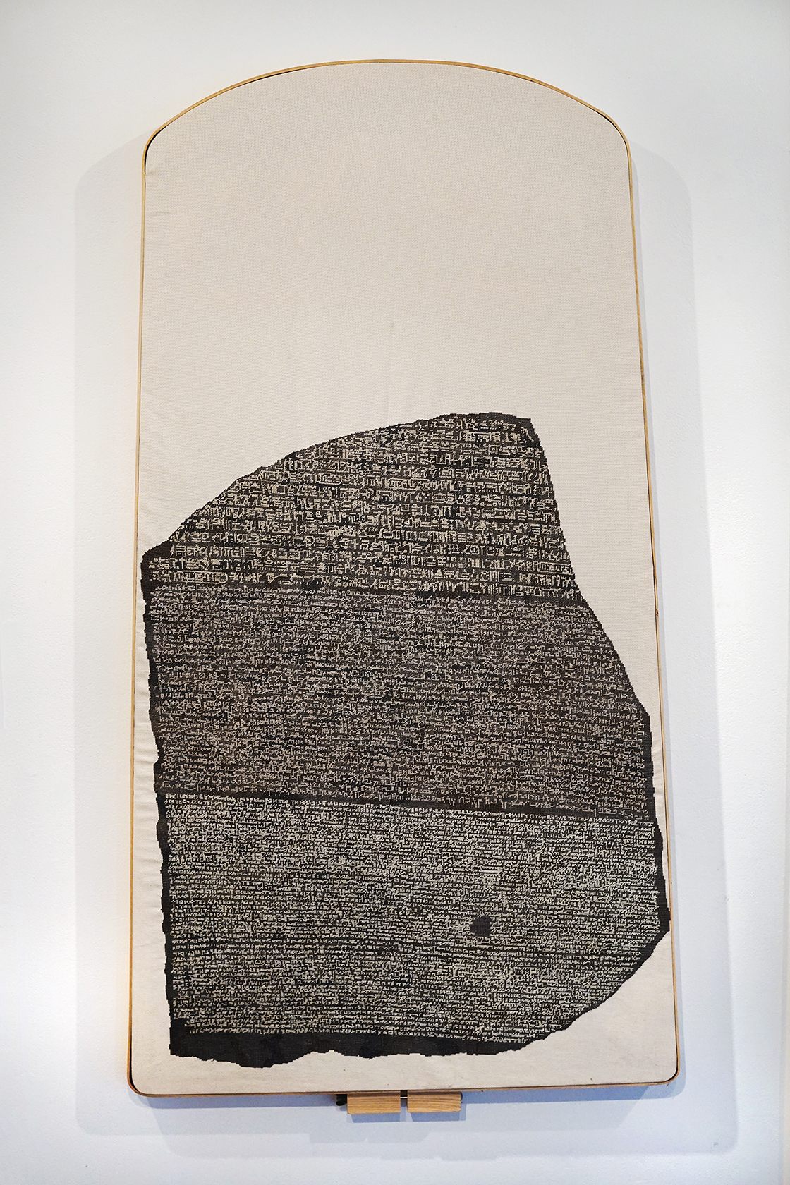 A large embroidery frame resembling a tall boulder with cream-colored cloth and black and white embroidery resembling densely written text