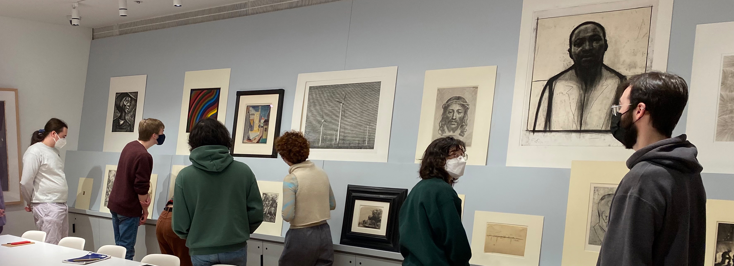 Masked students gather in a study gallery with artworks on the wall and a table