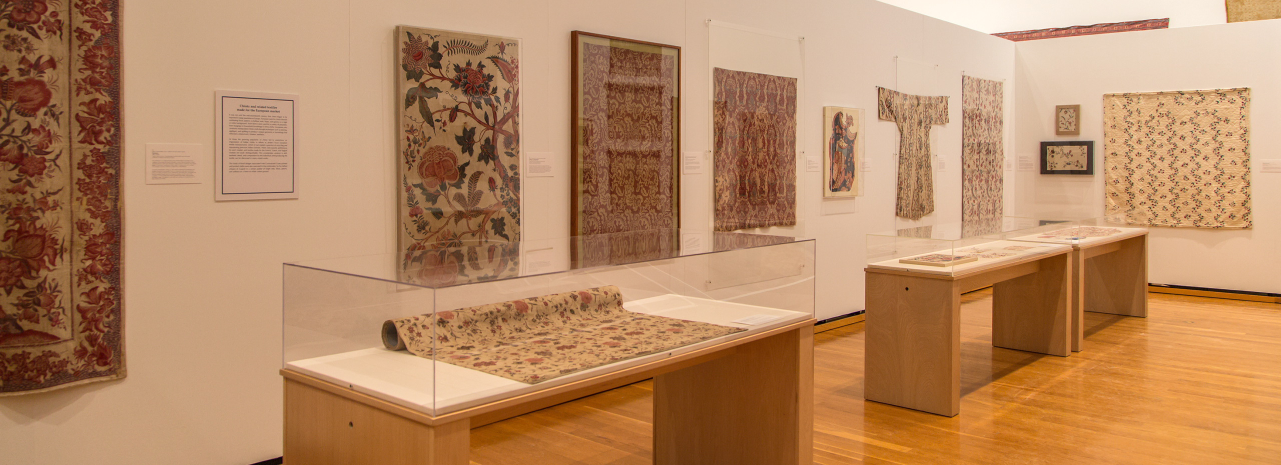 Colorful textiles of different shapes hang on gallery walls and are displayed in cases