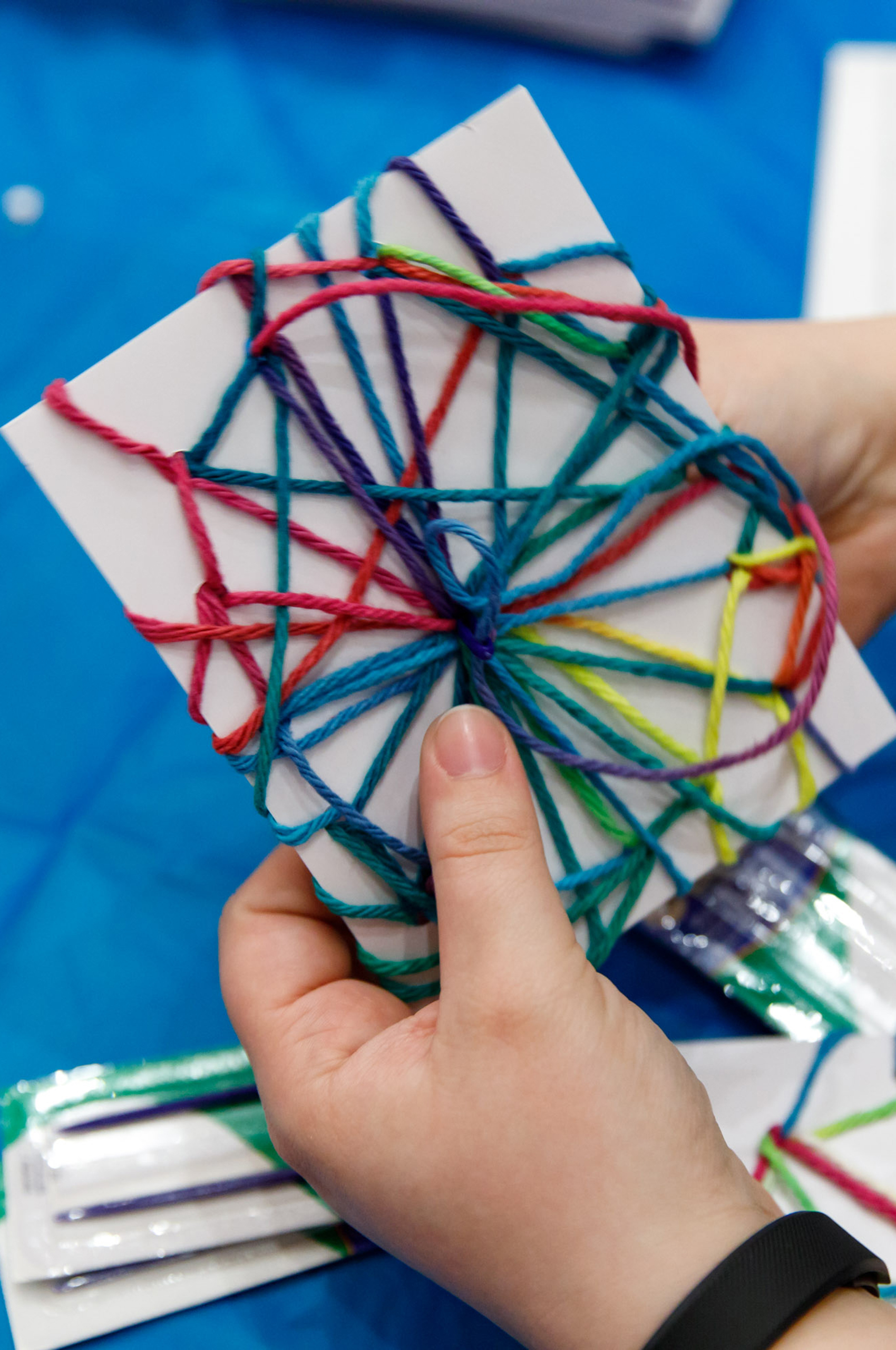 A child's hands hold a white card with a web of colorful yarn around it