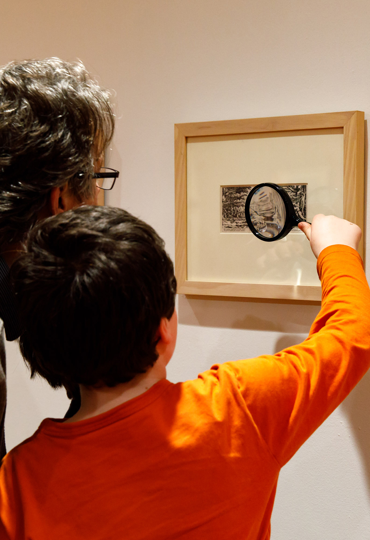 A man and boy look at a framed etching through a magnifying glass