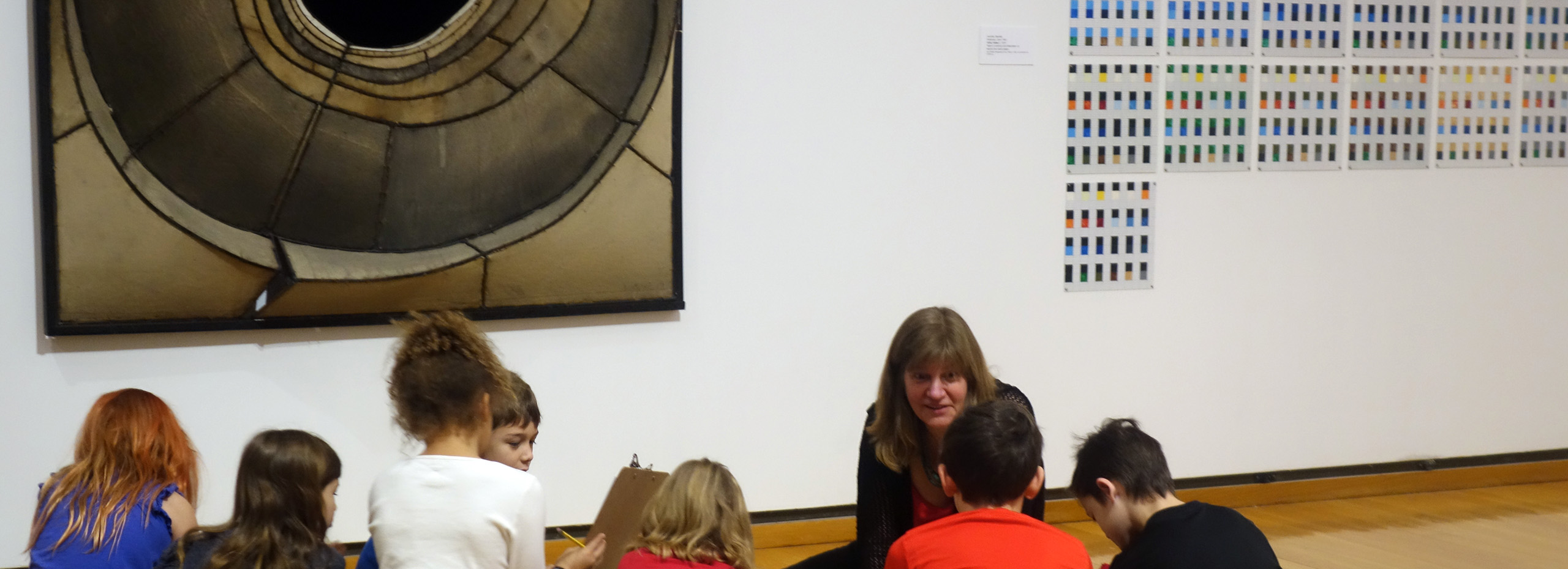 A woman teaches a group of young children in an art gallery