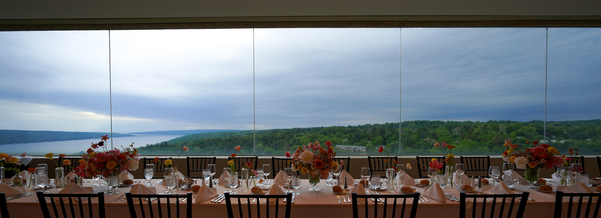 A sweeping landscape and lake from the windows of a large room set with a banquet table with flowers