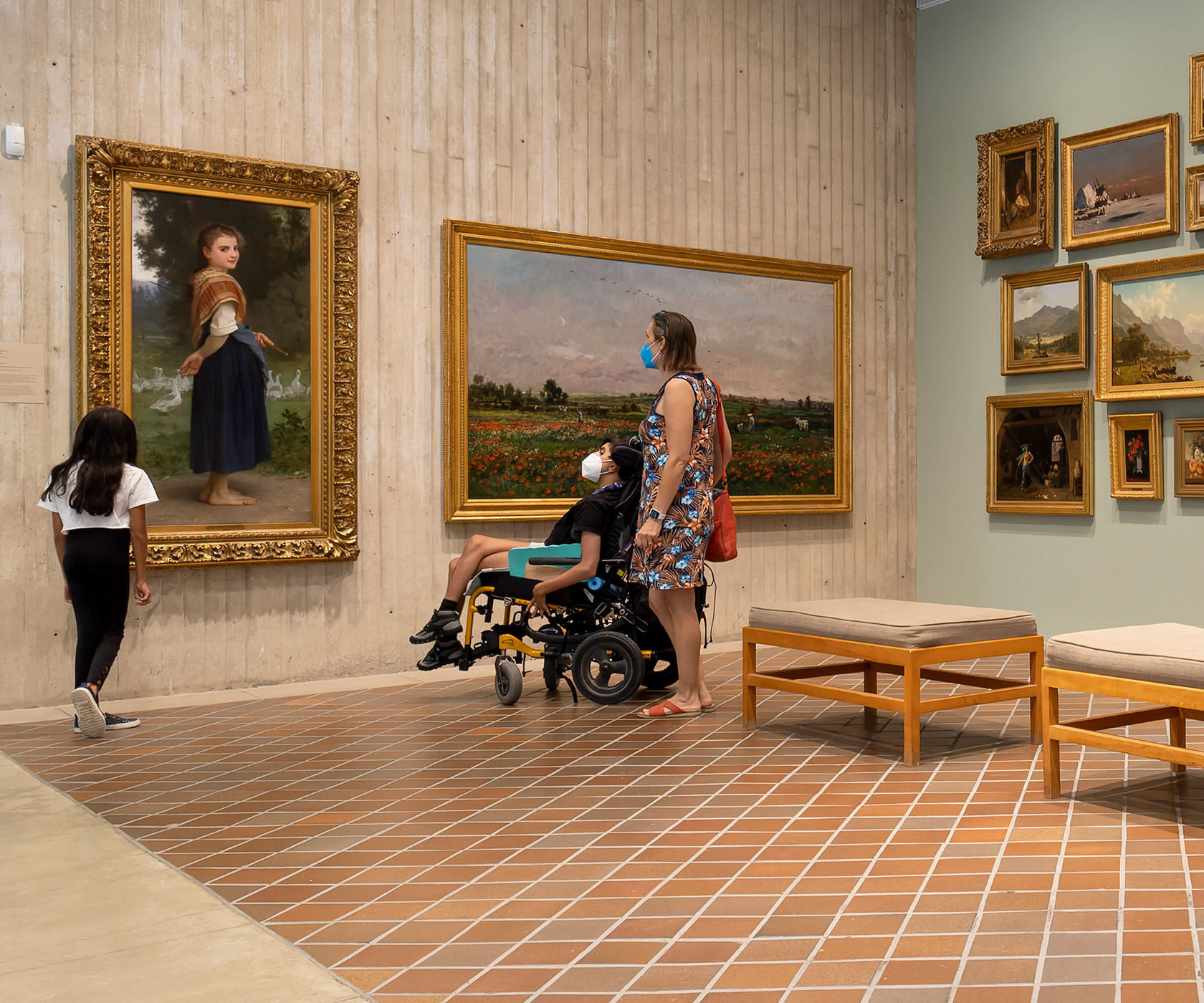 A woman, a child, and a person in a wheelchair look at large oil paintings in a museum gallery
