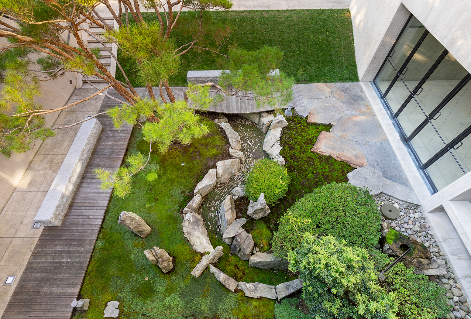 Looking down on a courtyard garden with rock formations and green trees, scrubs, moss.