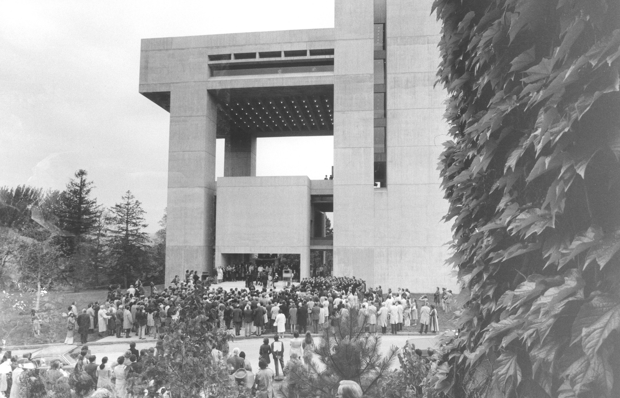 A black and white photo of a large cantilevered building with a crowd gathered in front of the entrance
