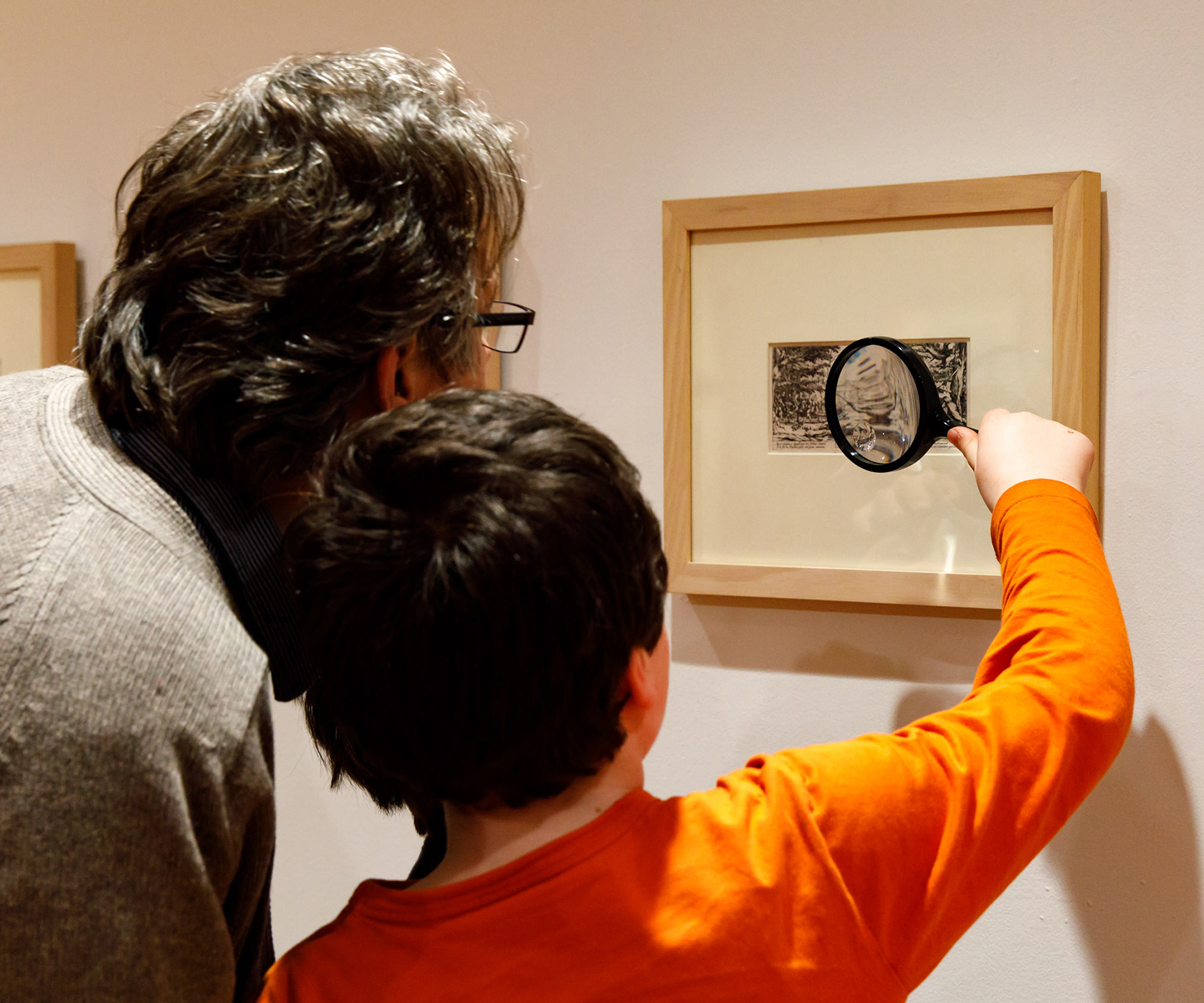 A man and boy look at a framed etching through a magnifying glass