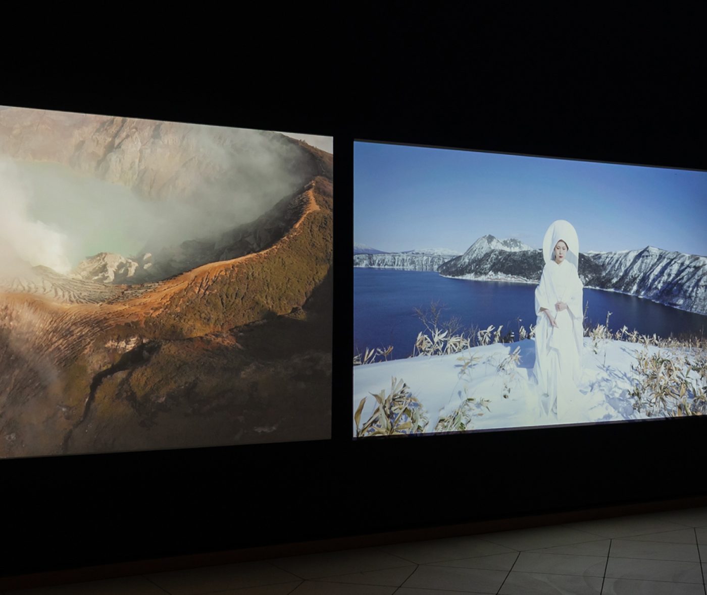 A three-channel video projection shows a central woman in white in and beside landscapes of clouds, mountains, and bodies of water