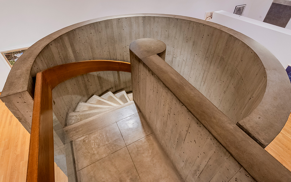 The top of a concrete spiral staircase with a wooden railing