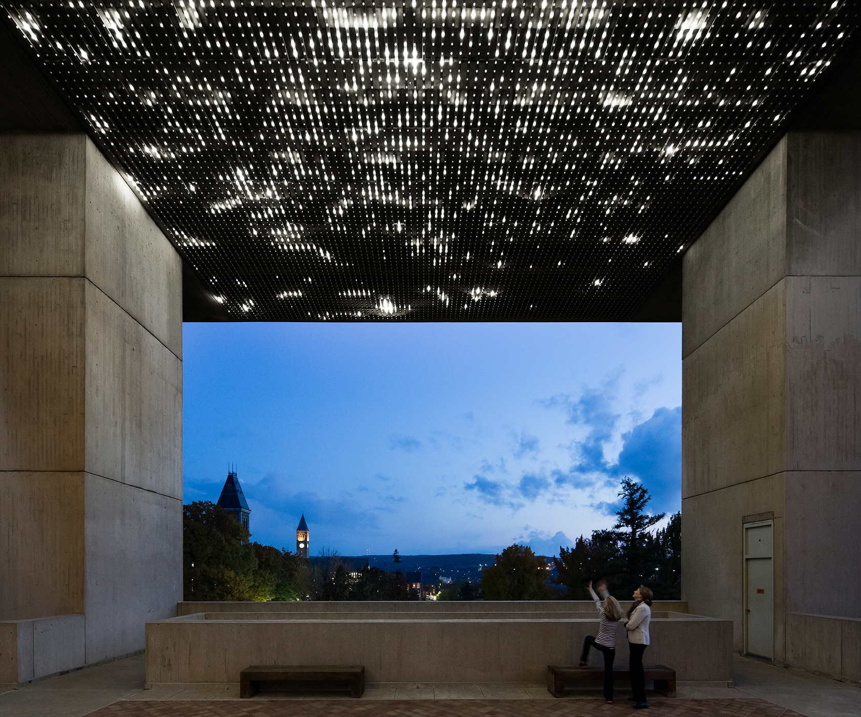 The ceiling of an outdoor courtyard is covered with thousands of white lights while figures below point up at twilight