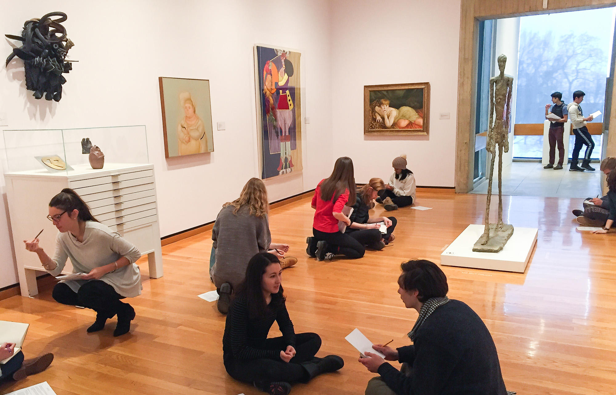 A group of college students sitting on the floor of a museum art gallery working on an assigment