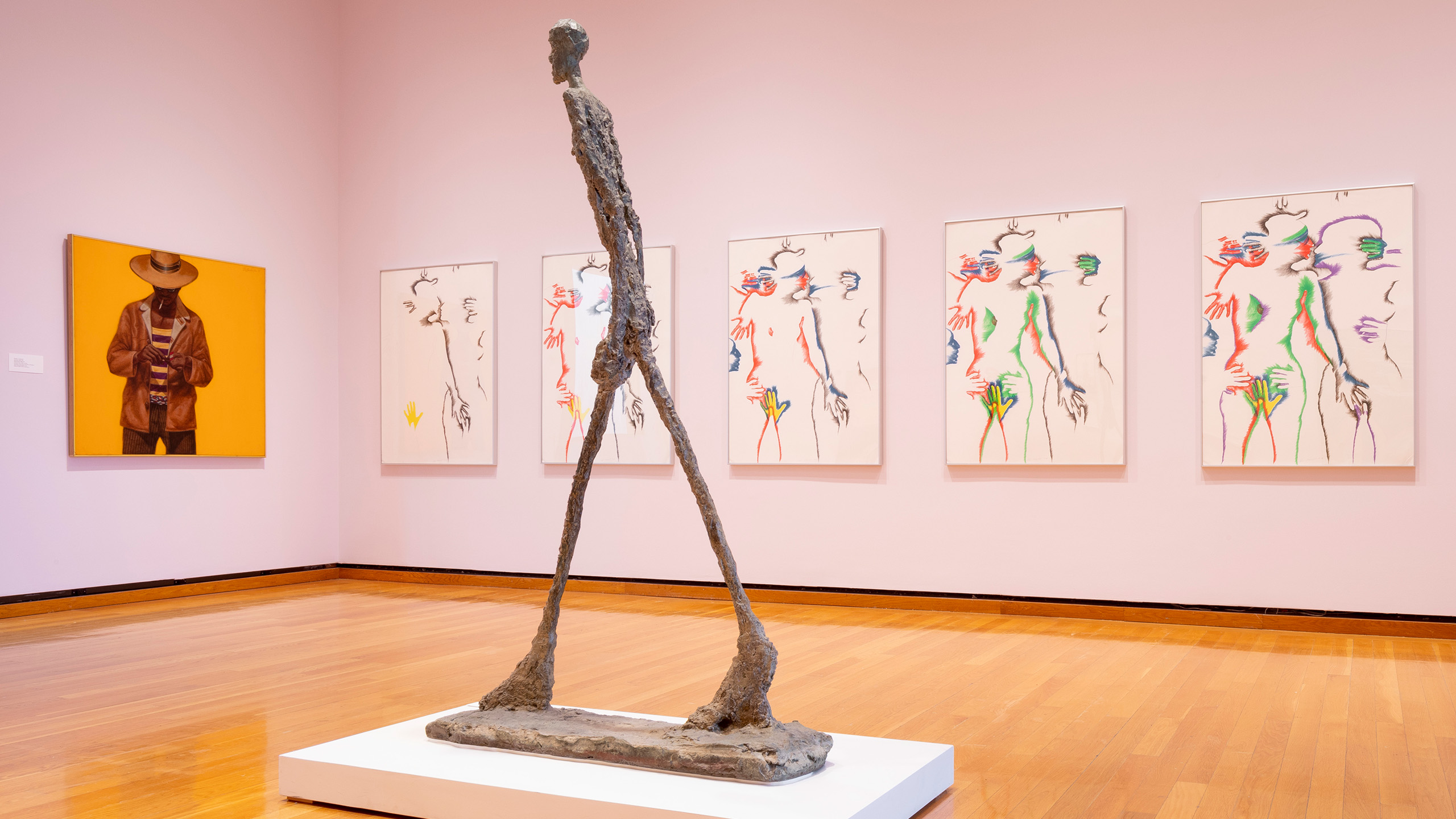 A tall figural statue in a gallery with colorful framed artworks on the walls