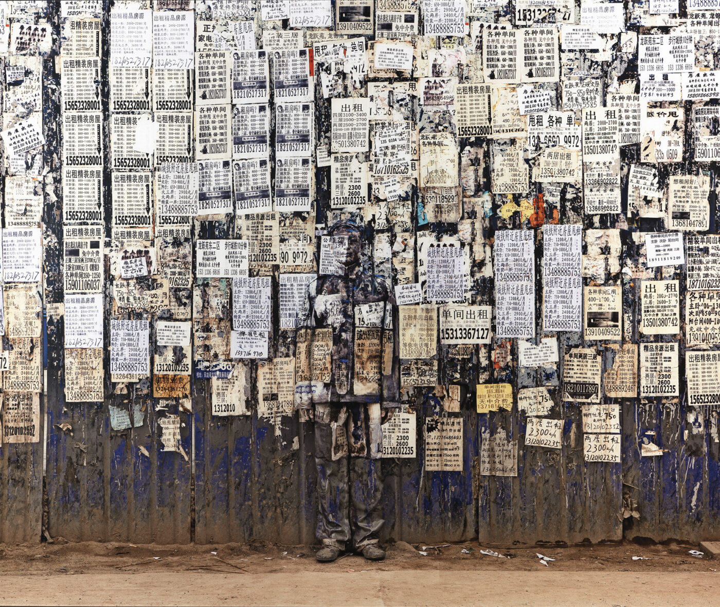 A man's body is camouflaged by posters covering a dirty wall