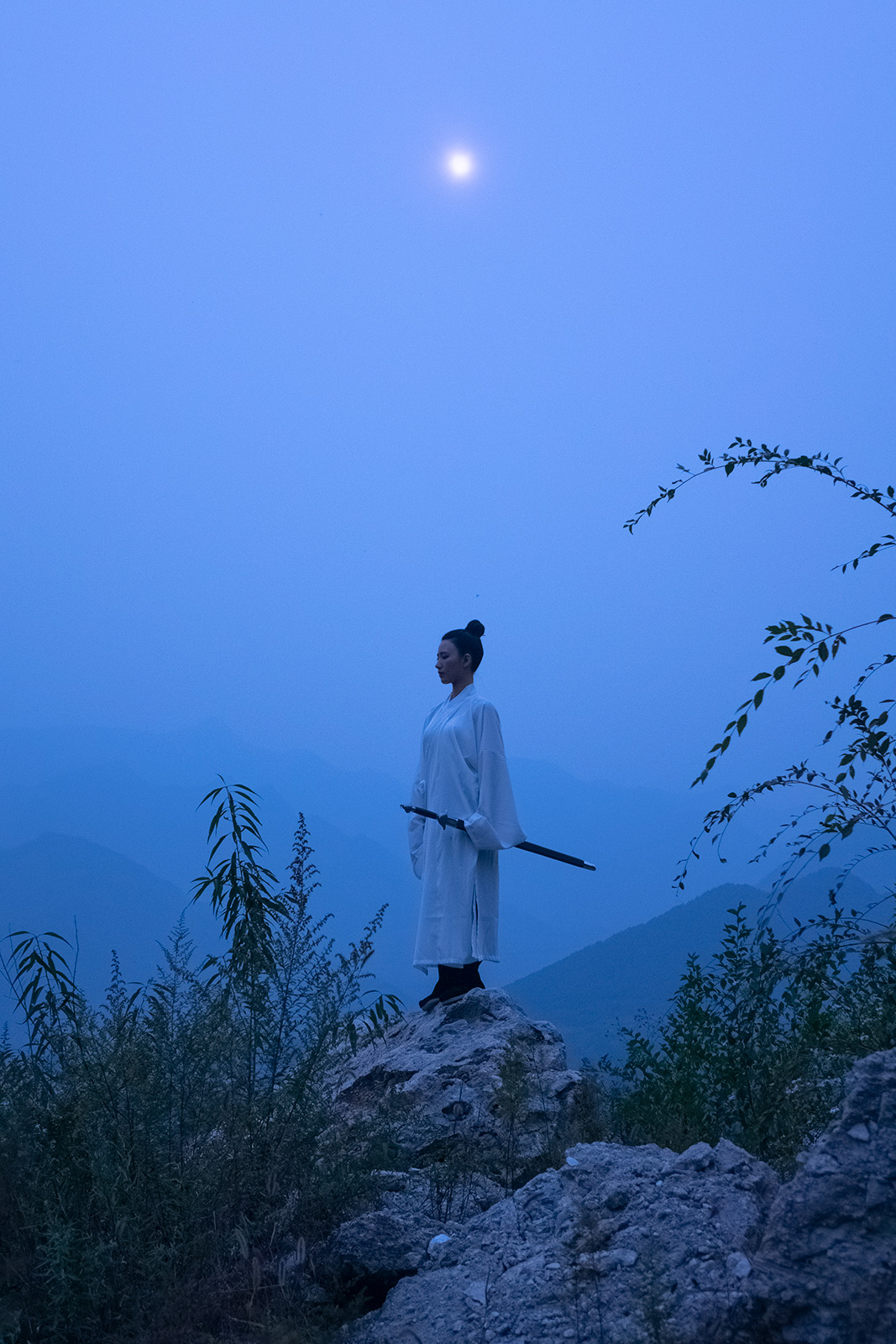 A samurai figure stands outside beneath an object in the evening sky