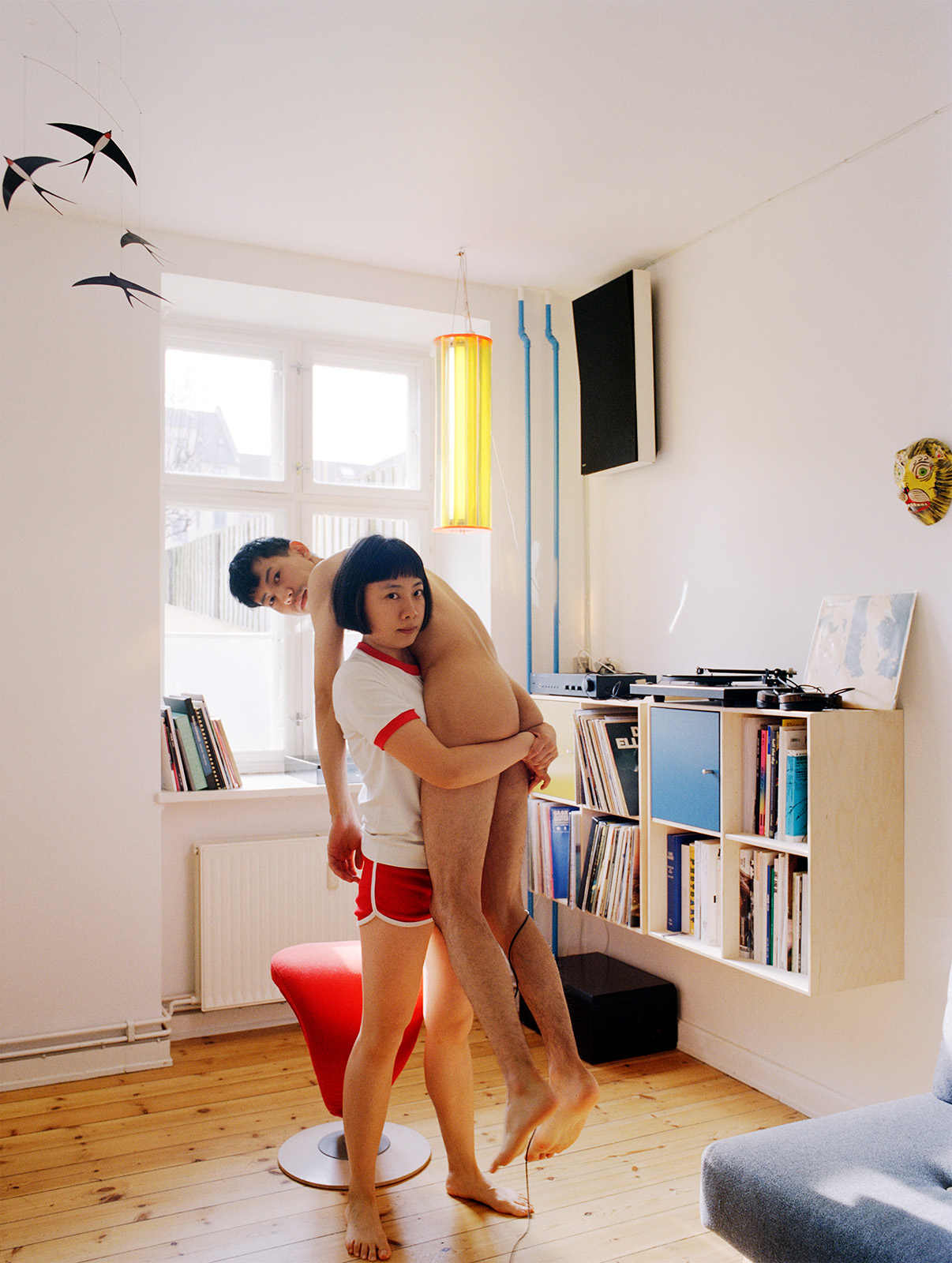 A woman lifts up a naked man in a room with book shelves