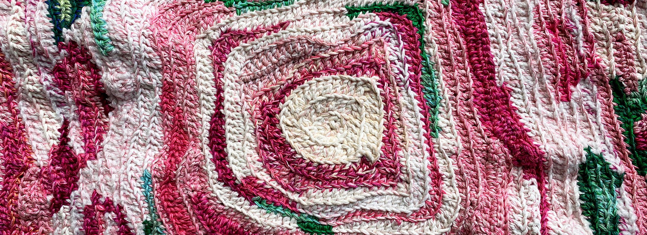 A closeup of a roselike form crocheted in whites, pinks, and green