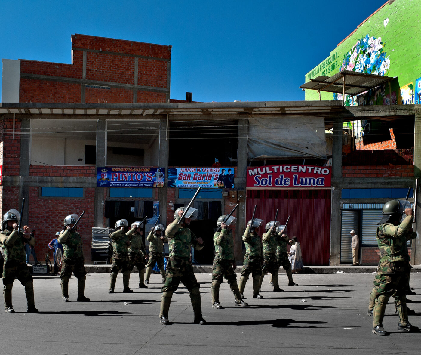 Soldiers stand on a street of colorful abandoned storefronts under a bright blue sky
