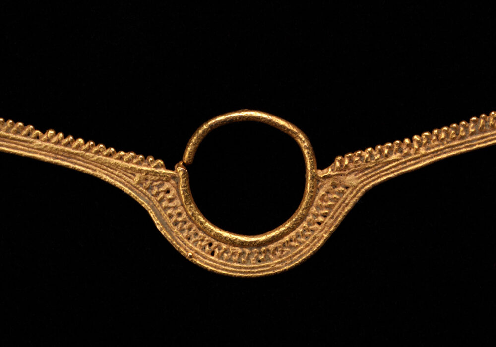 A long gold-tone metal object with an open circle at its center