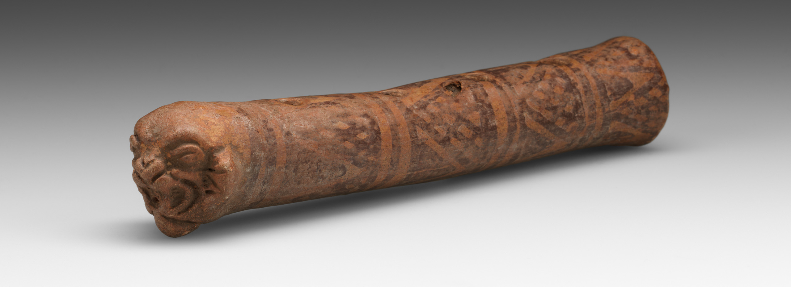 A wood flute carved with an animal face on one end and marked with a geometric pattern
