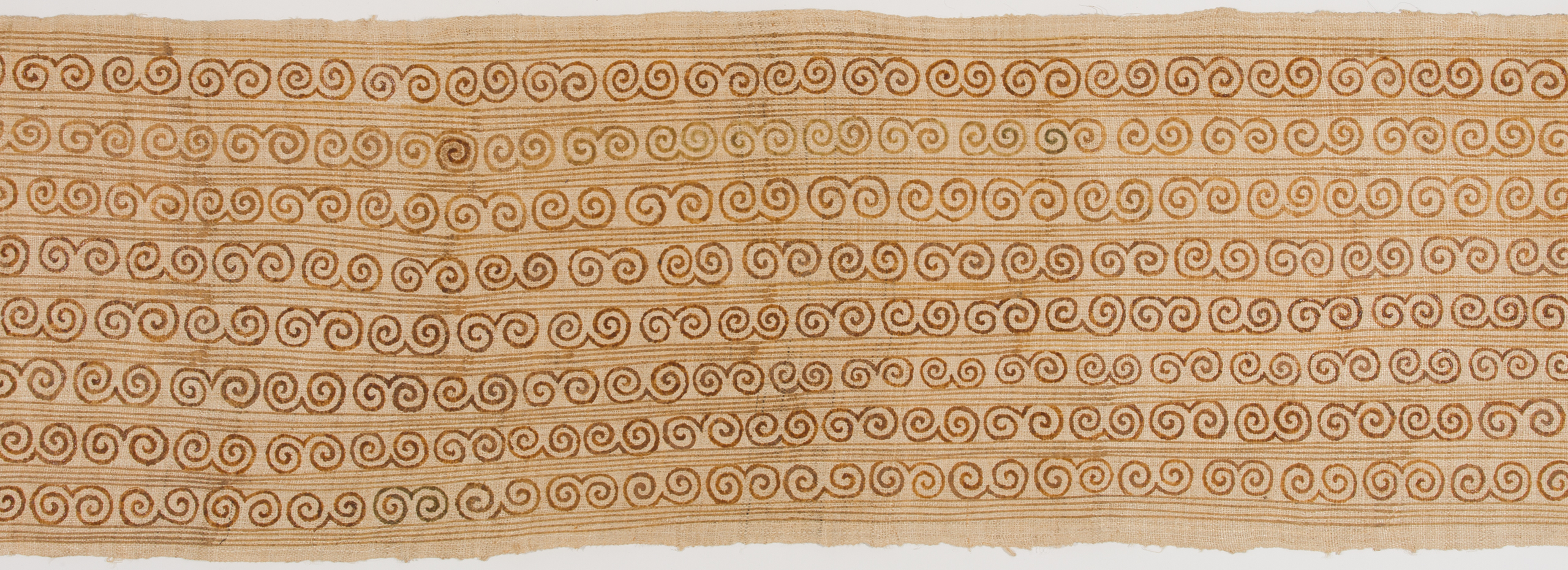 Portion of a horizontal light brown cloth with a darker brown pattern of curled and straight lines