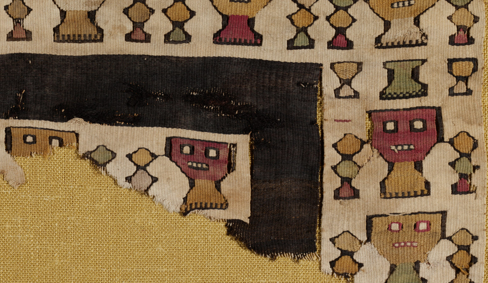 A fragment of a fringed brown textile with figures and geometric shapes dyed in different colors