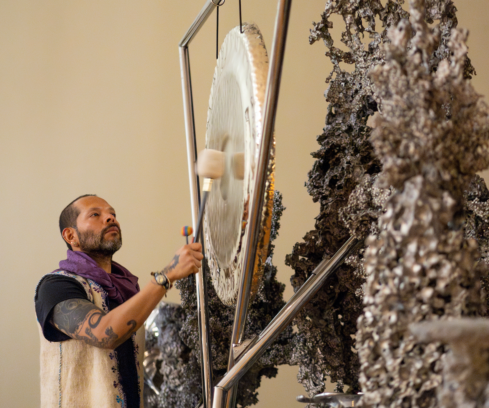 Artist Guadalupe Maravilla strikes a silver gong with a white mallet as part of a sound bath program