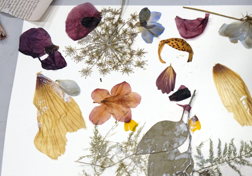 A workshop table with dried flowers, plants, paper, and brushes