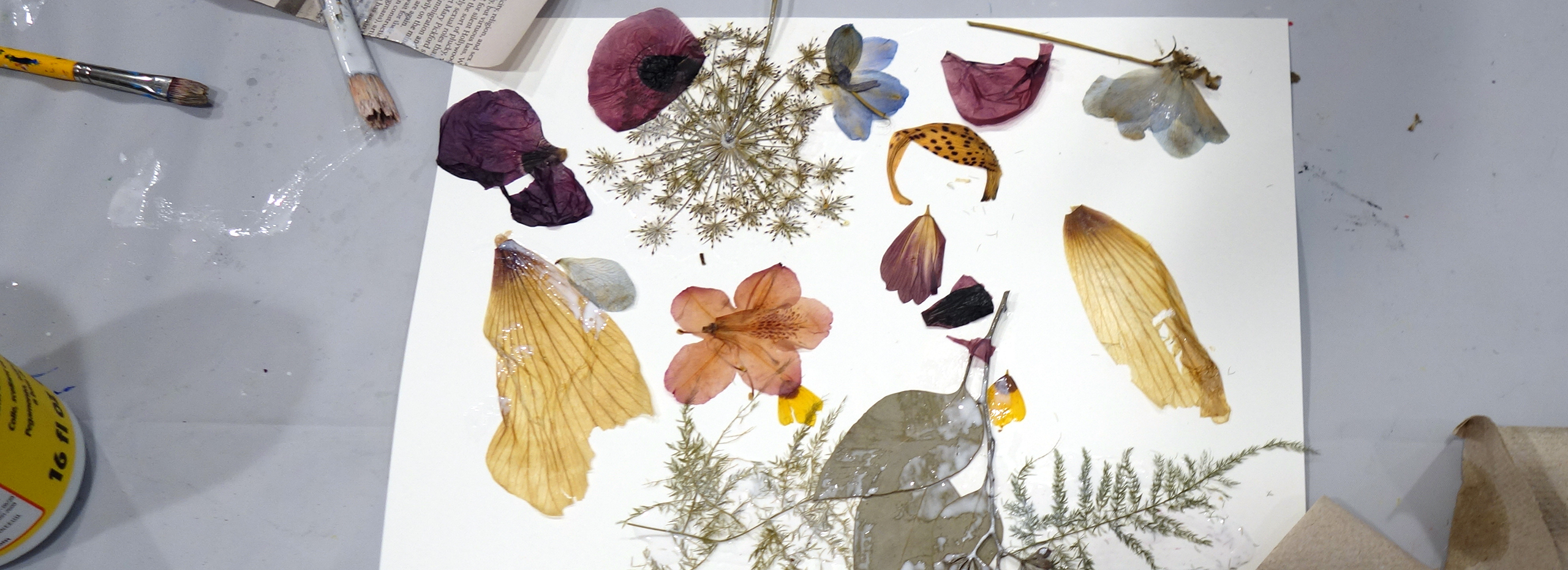 A workshop table with dried flowers, plants, paper, and brushes