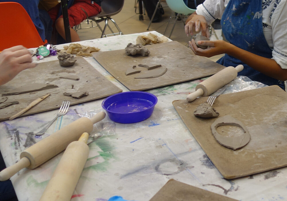 Students make clay sculptures with their hands at a studio table