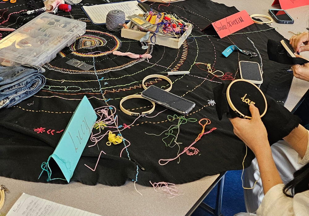 A large table holds items for sewing as a young woman mends an item