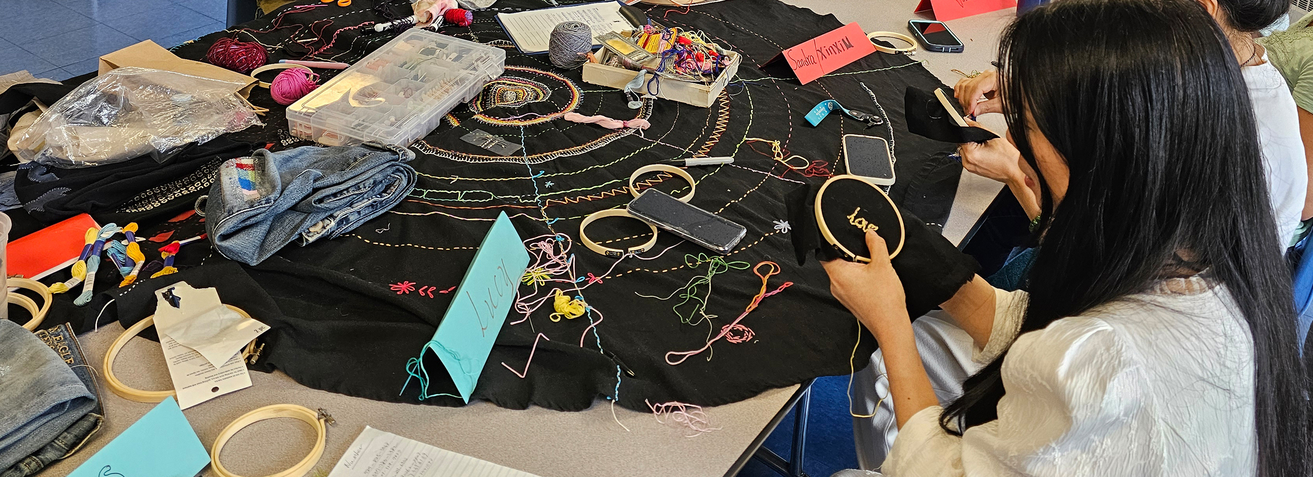 A large table holds items for sewing as a young woman mends an item