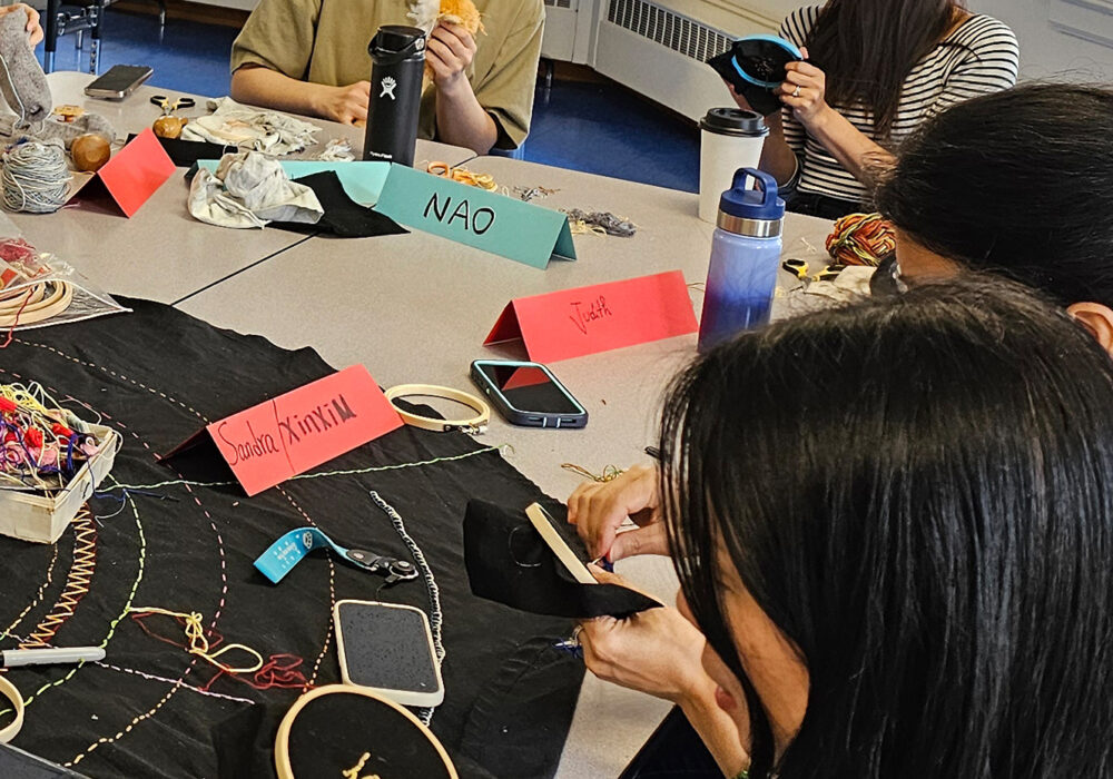 Students sew around a table covered with different items for sewing