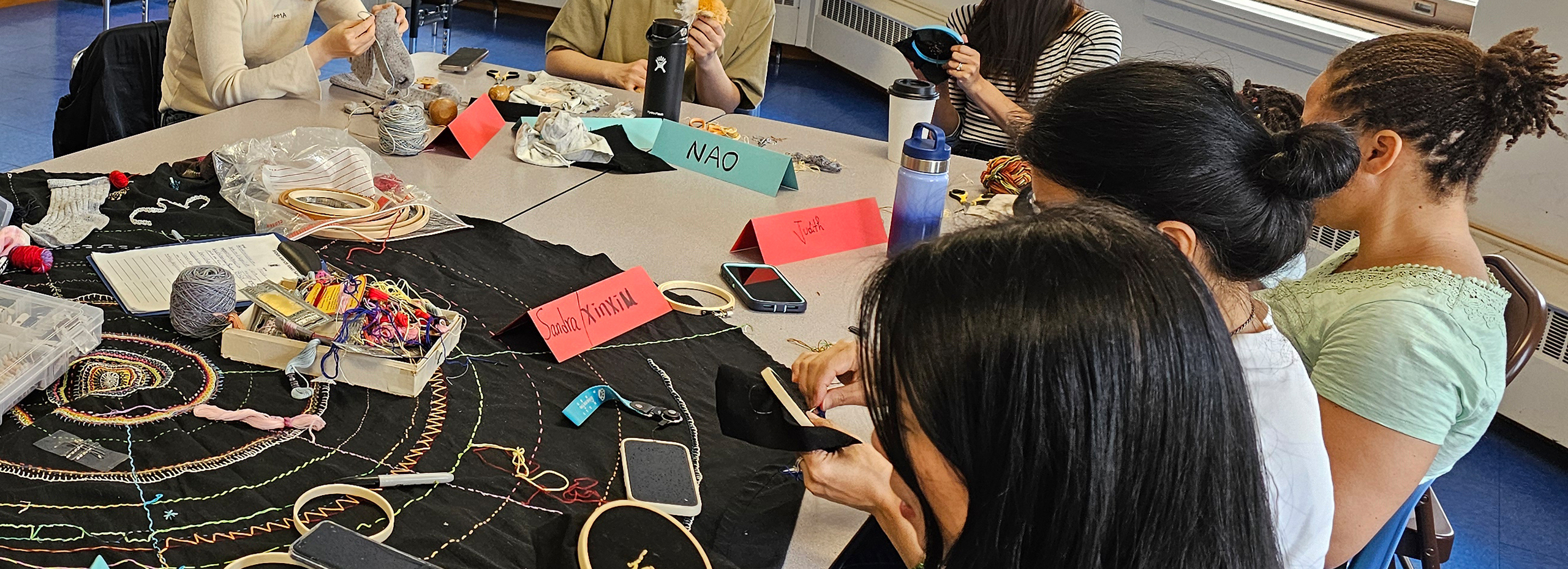 Students sew around a table covered with different items for sewing