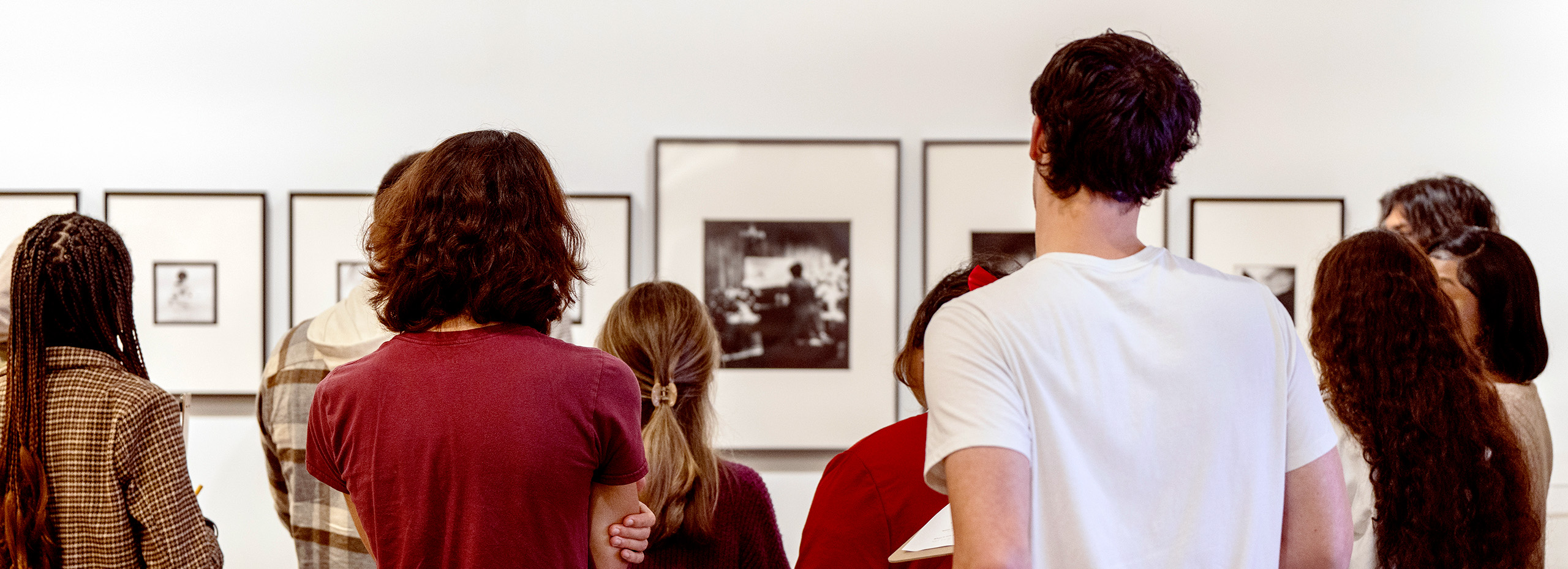 A group of students look at framed artwork on a white wall