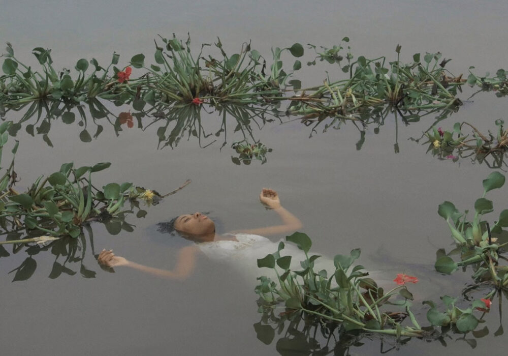 A Black woman in a white dress floats in a body of water full of flowers