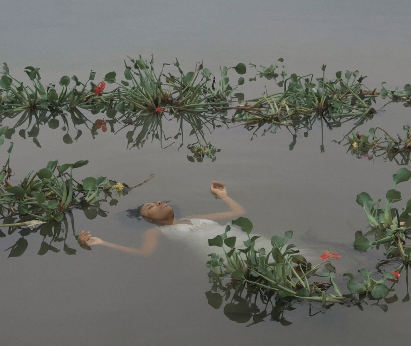 A Black woman in a white dress floats in a body of water full of flowers