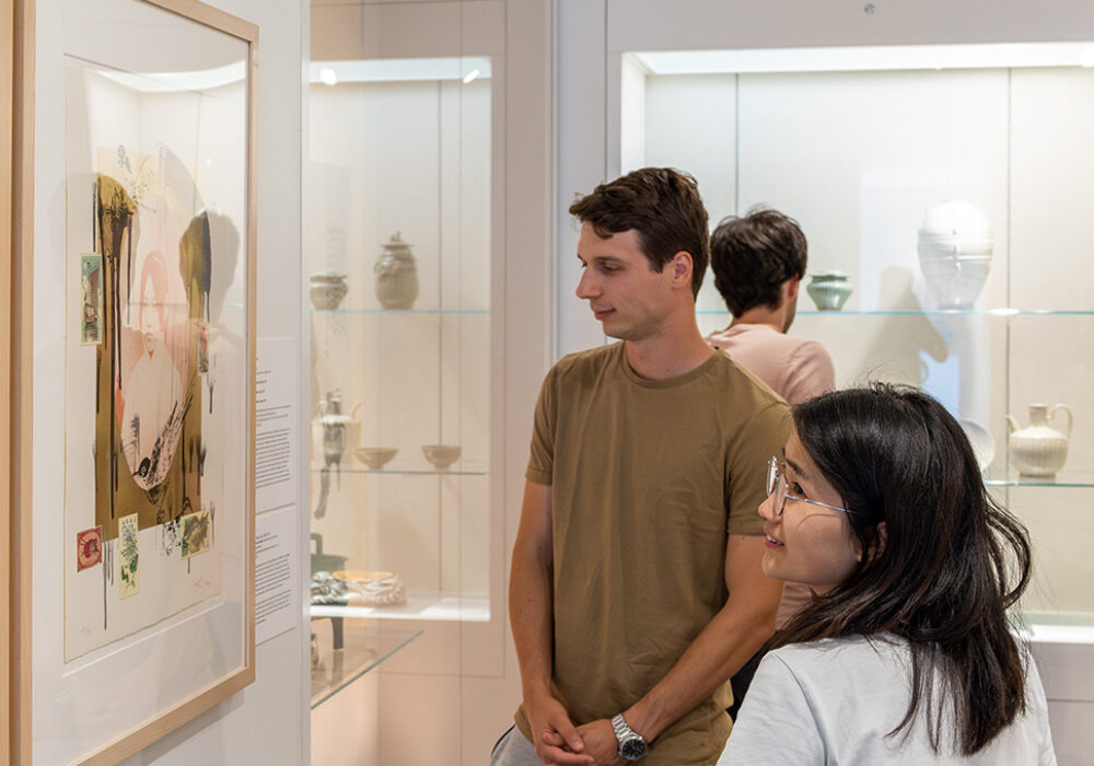 People look at artworks in display cases at a museum