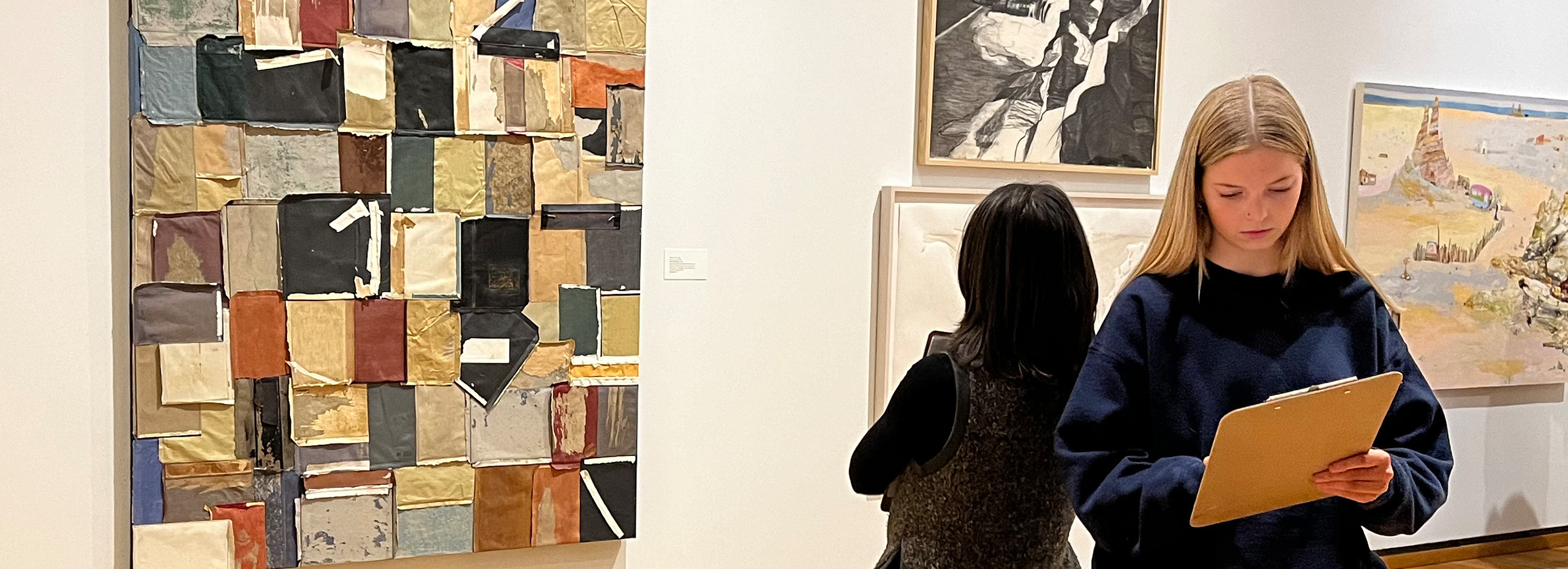 People look at art and write on clipboards in a museum gallery