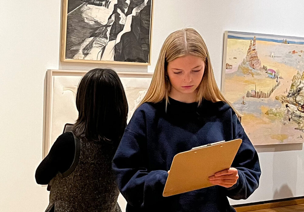 People look at art and write on clipboards in a museum gallery