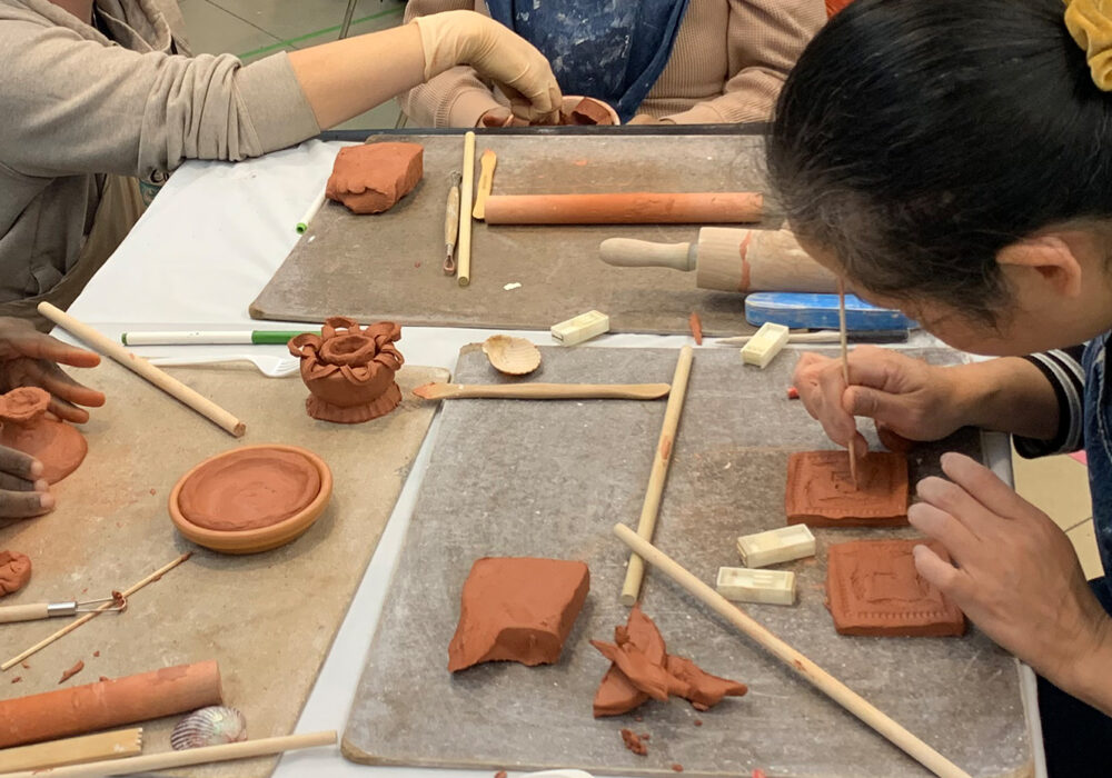 People work on small ceramic sculptures at a table