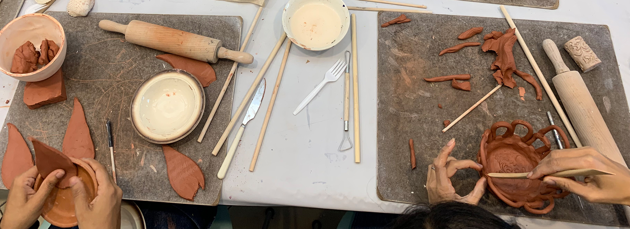 Hands work on small ceramic sculptures at a table