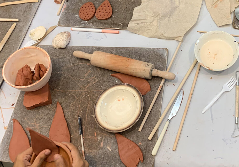 Hands work on small ceramic sculptures at a table