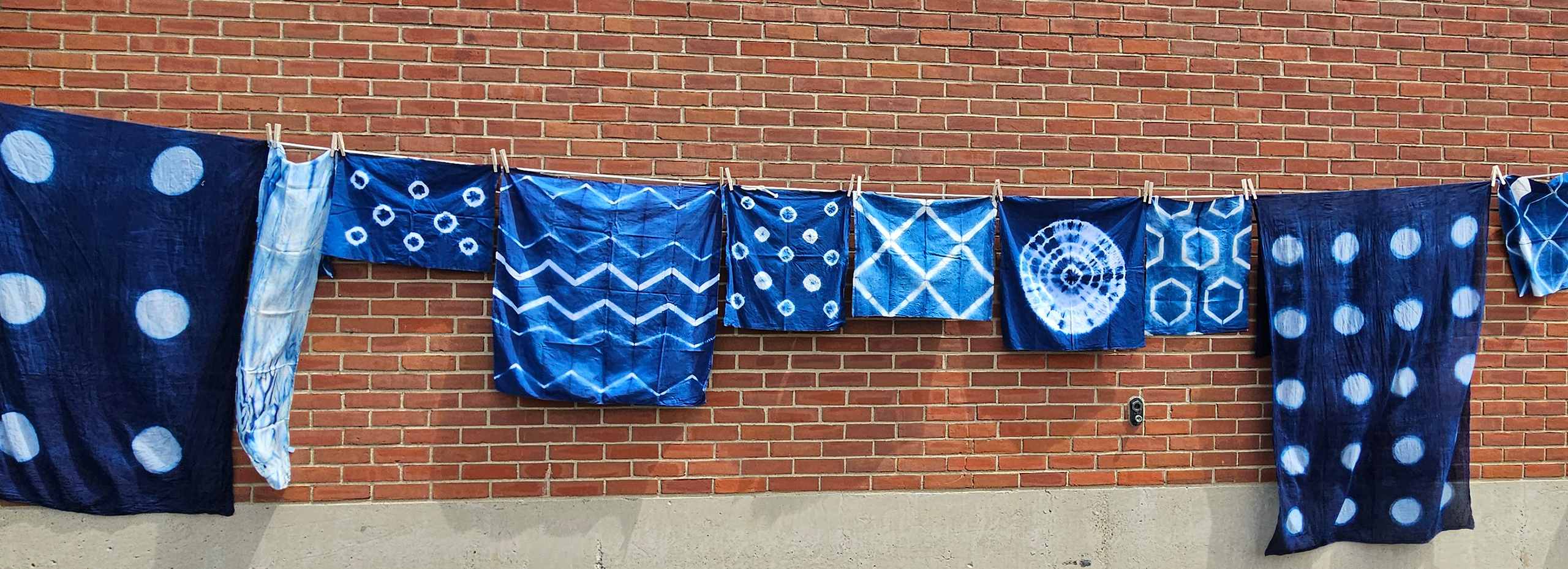 A clothesline of blue and white garments hangs against a brick wall