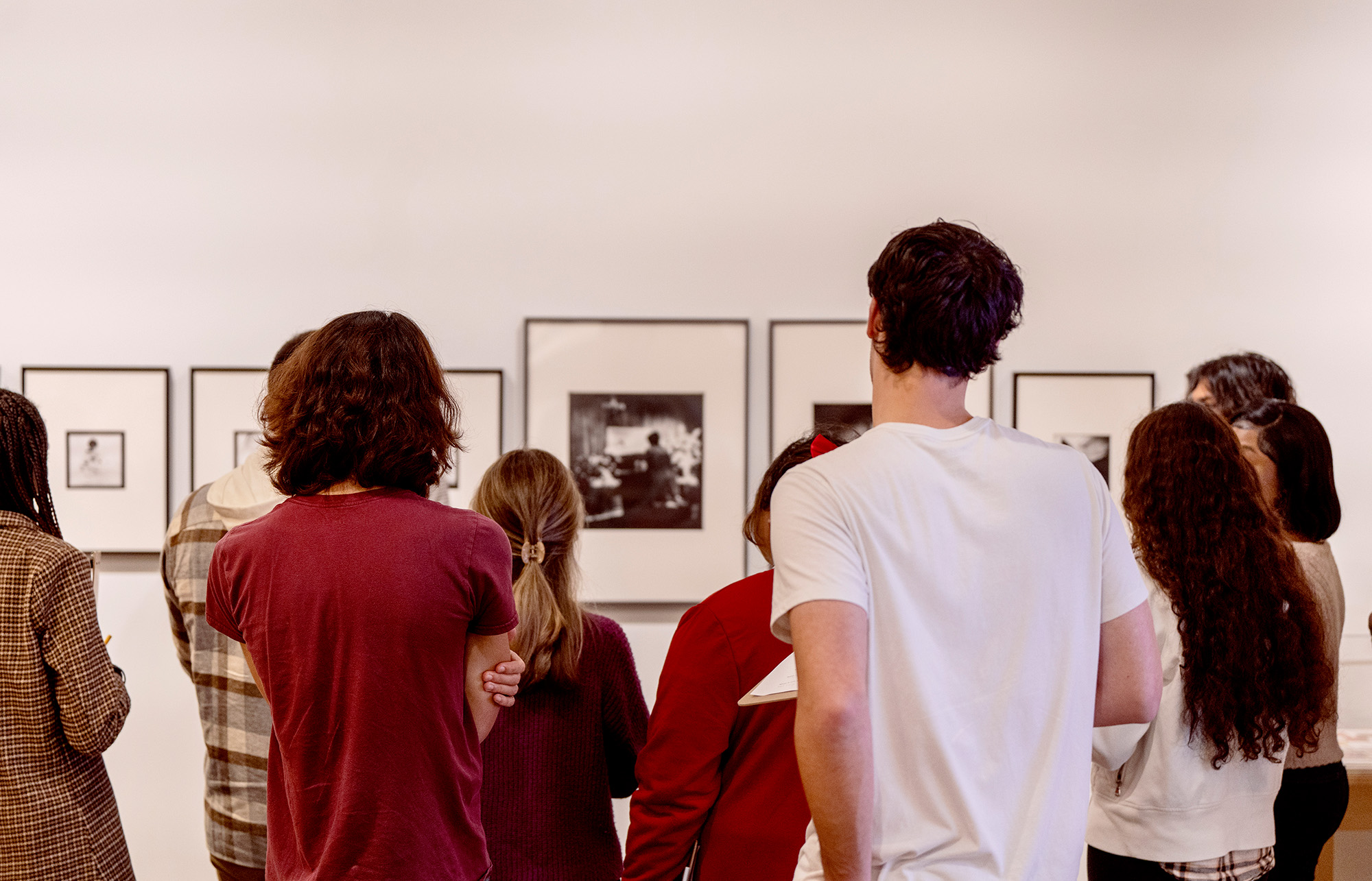 A group of students look at framed artwork on a white wall