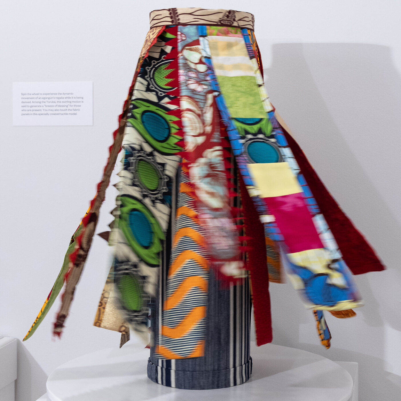 A cylinder with colorful strips of fabric spins on a rotating white disc